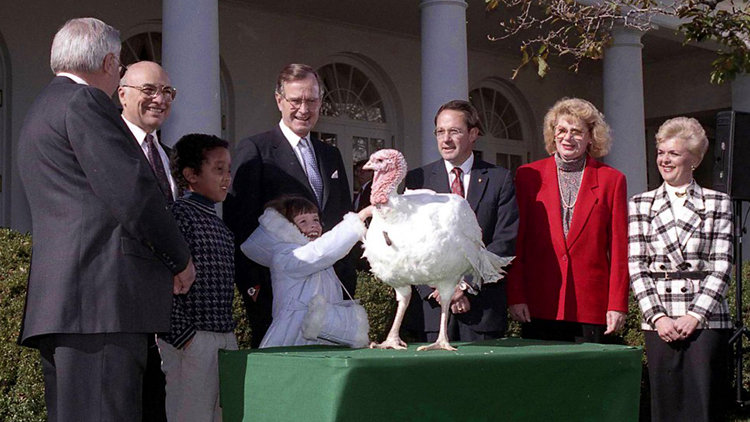 George Bush standing with others behind a table with a turkey on it.