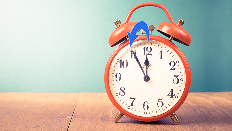 retro analog alarm clock reading 11:55 on a wooden surface