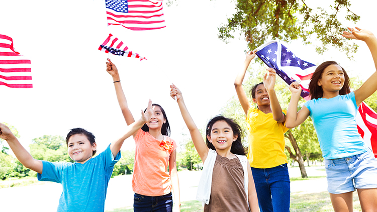 Diverse group of Hipanic and African American friends wave American flags at Independence Day parade in their community. They are each waving and holding a flag. They are dressed casually.