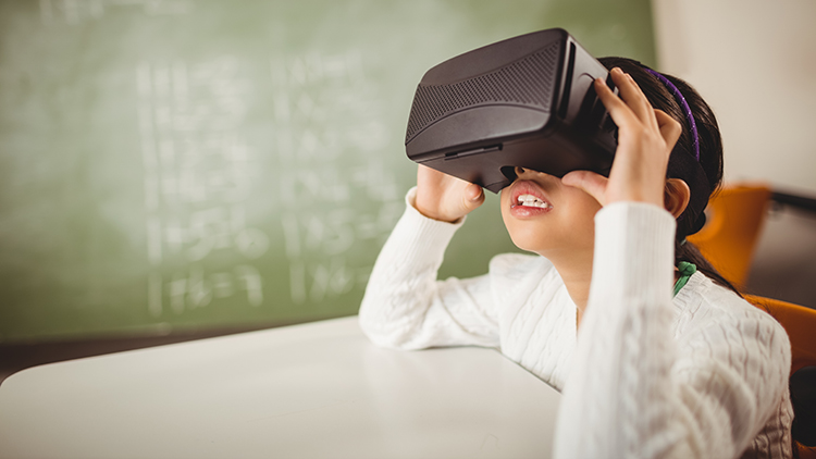 Head and shoulders view of an Asian girl wearing virtual reality glasses sitting in a classroom