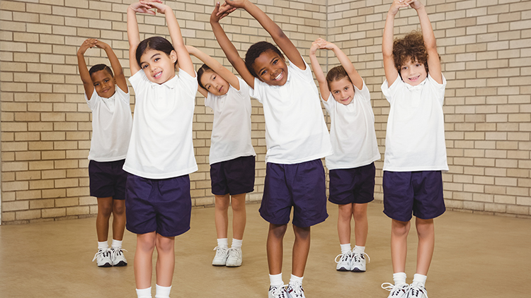 Grupo diverso de niños de edad elemental que ejercitan en el gimnasio, de pie, de longitud completa