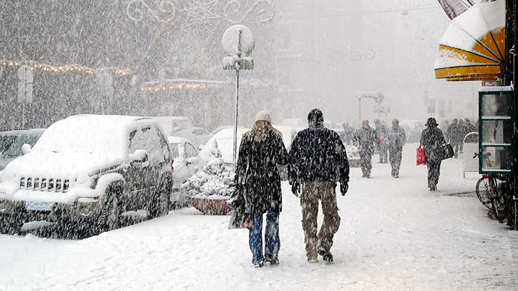 People walking down sidewalks in a snowstorm in a city.